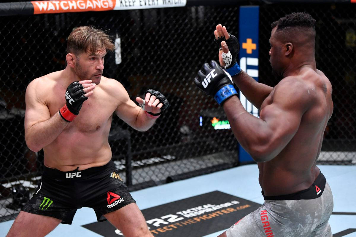 UFC 桌布 壁紙 — 兩名肌肉發達的MMA拳手穿著黑色和灰色短褲，在明亮的場館燈光下進行緊張的籠中比賽，交換拳套。