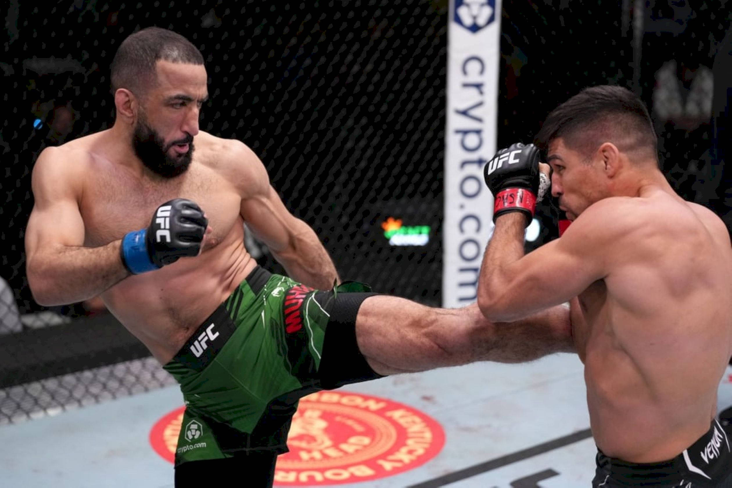 MMA 桌布 壁紙 — 兩名肌肉發達的UFC拳手在八角籠中交鋒，一人使出高踢，另一人則在緊張的戰鬥時刻進行阻擋。