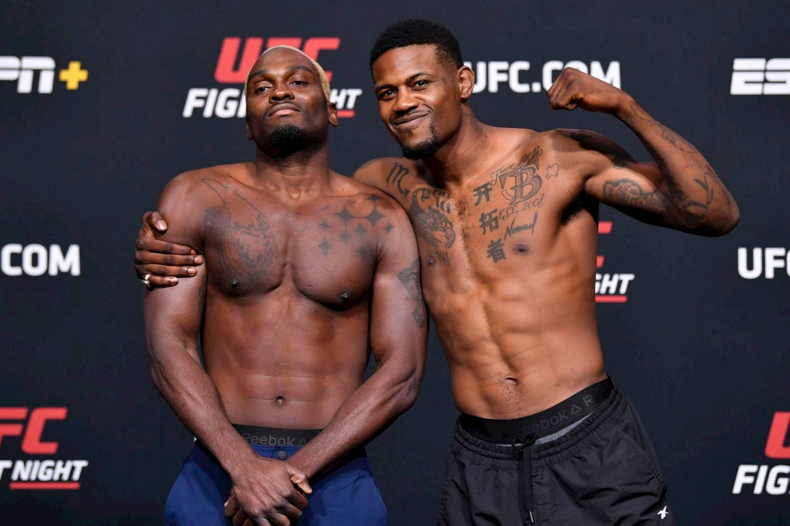 UFC 桌布 壁紙 — 兩名肌肉發達的UFC拳手在品牌背景前自信地擺姿勢，紋身清晰可見。