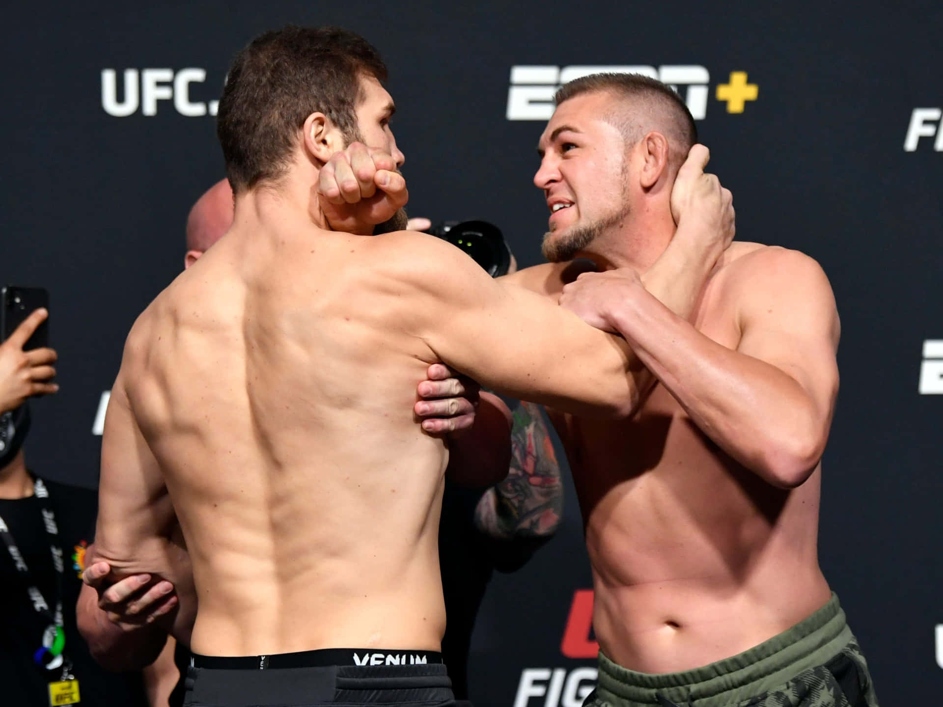 MMA 桌布 壁紙 — 兩名肌肉發達的UFC拳手在品牌背景前以賽前稱重姿勢激烈纏鬥。