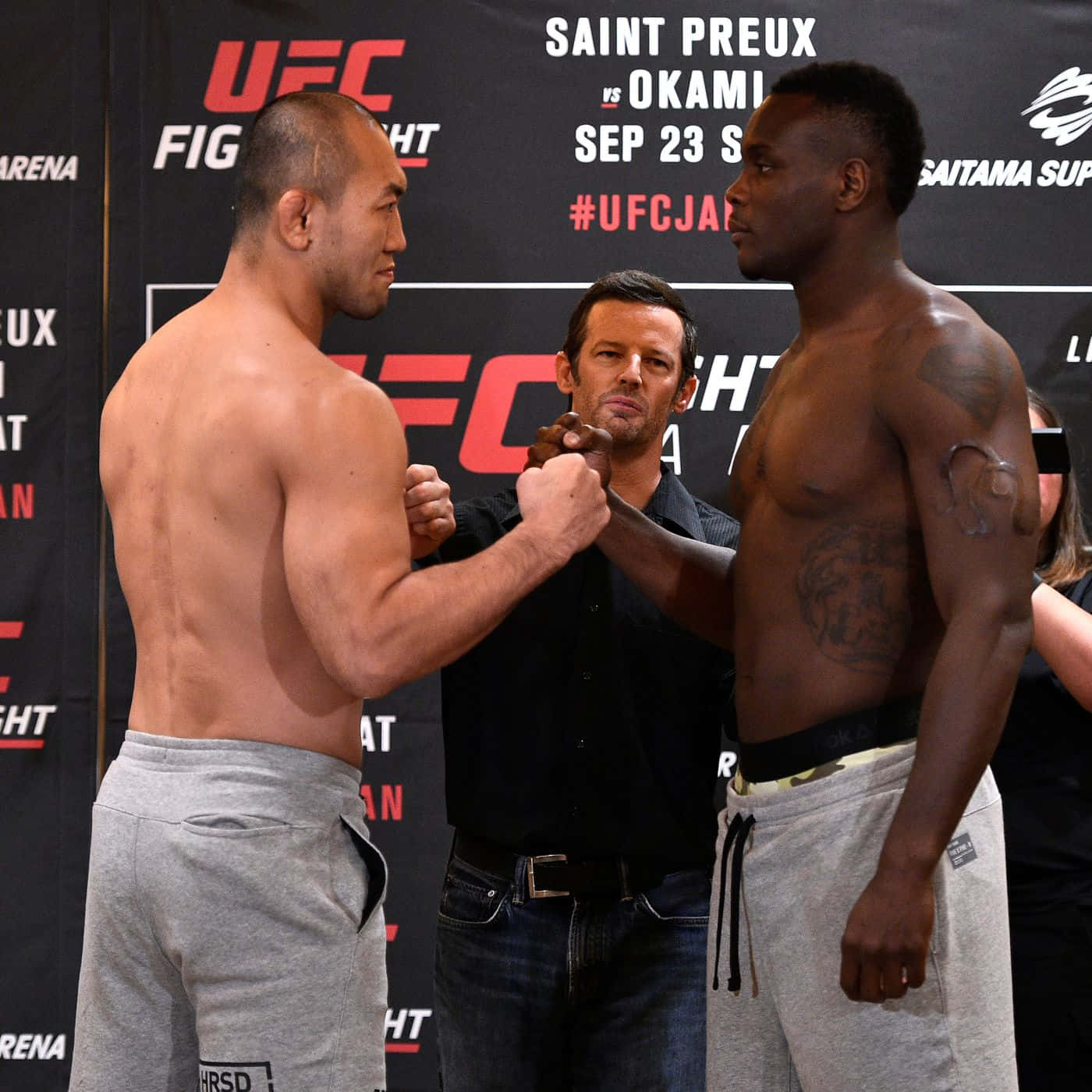 UFC 桌布 壁紙 — 兩名肌肉發達的UFC拳手在品牌背景前，由裁判隔開，於稱重儀式上對峙。
