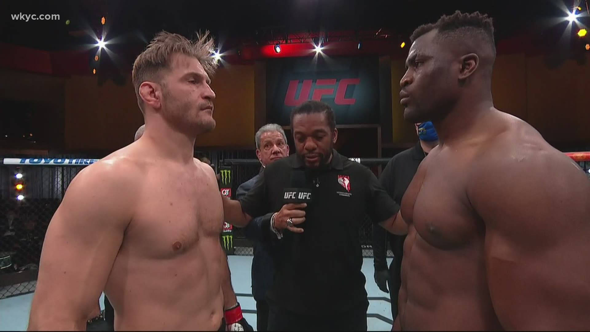 UFC 桌布 壁紙 — 兩名肌肉發達的UFC拳手在明亮的競技場燈光下於八角籠中對峙，中間有裁判。