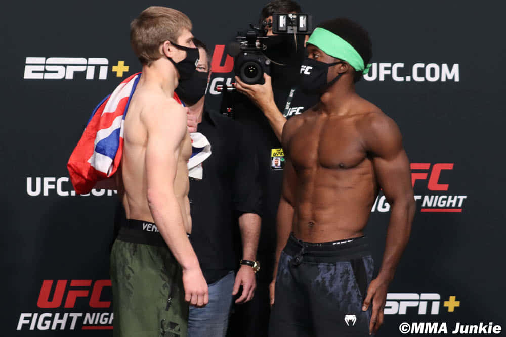 MMA 桌布 壁紙 — 兩名肌肉發達的UFC拳手在稱重時對峙，戴著口罩，攝製組捕捉緊張時刻。