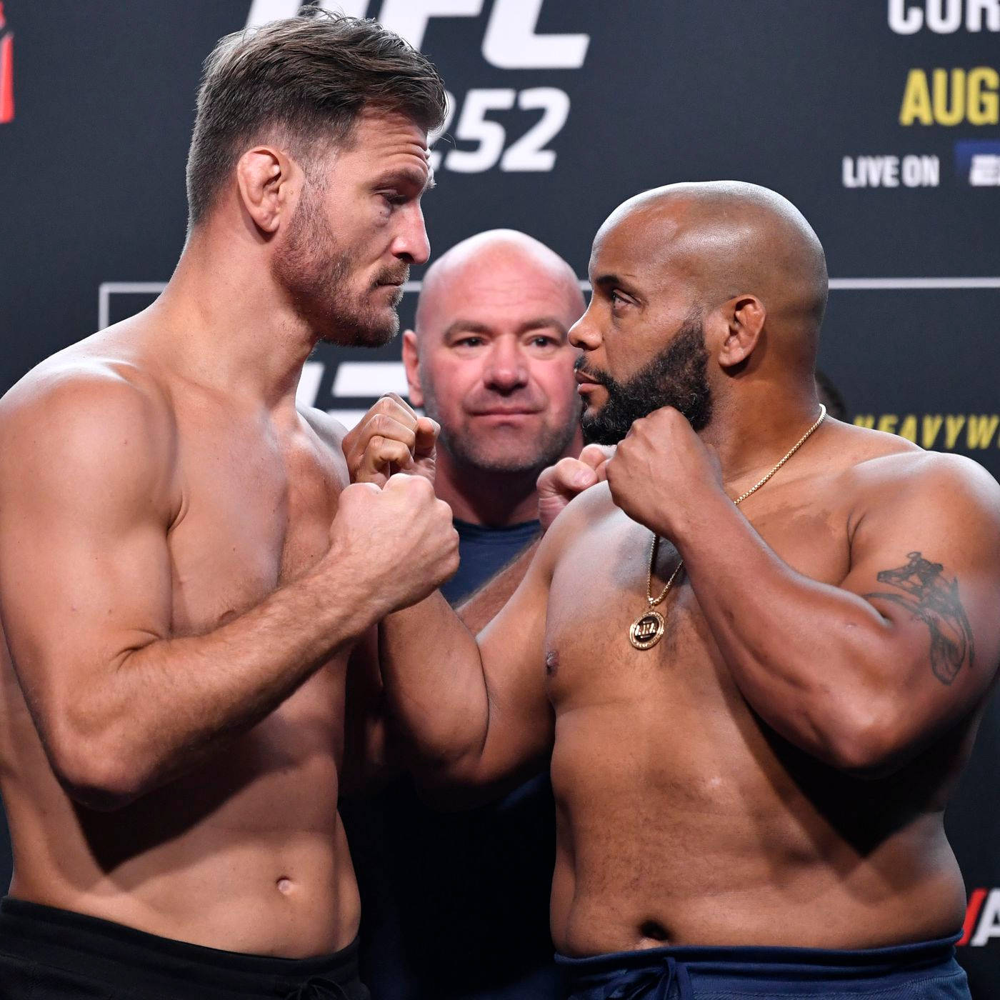 UFC 桌布 壁紙 — 兩名肌肉發達的UFC拳手在稱重活動中對峙，氣氛緊張，裁判在旁觀看。