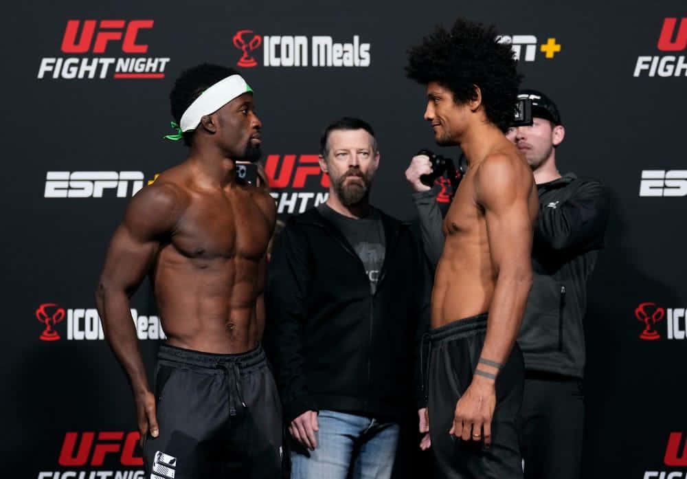 MMA 桌布 壁紙 — 兩名肌肉發達的UFC拳手在稱重活動中對峙，背景有品牌標誌，攝影師捕捉這緊張時刻。