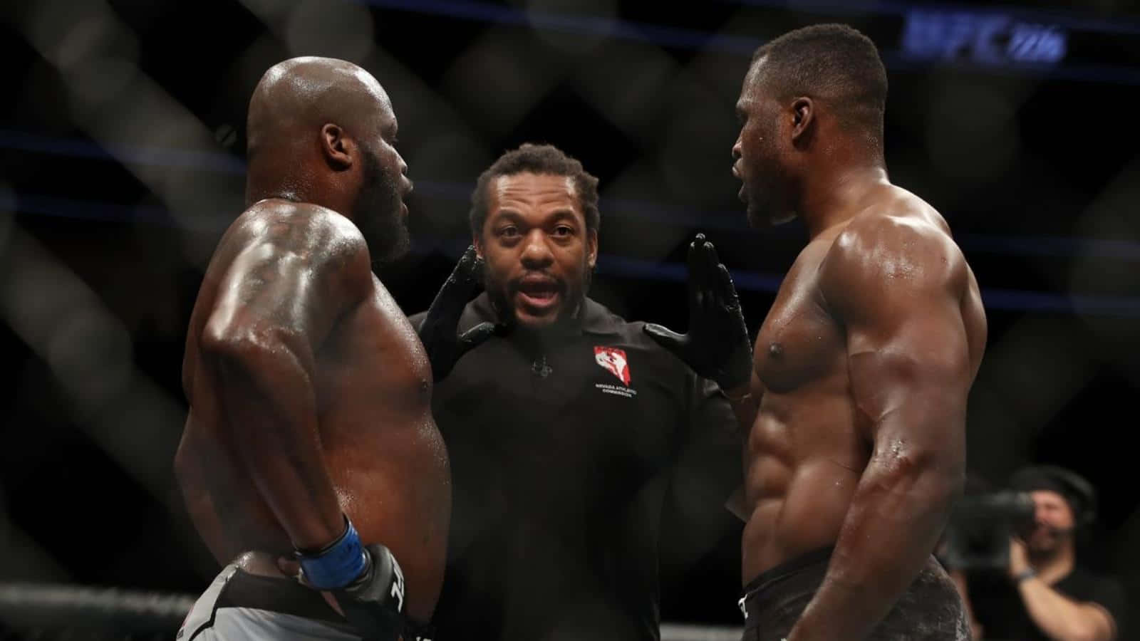 UFC 桌布 壁紙 — 兩名肌肉發達的拳手在MMA鐵籠中對峙，裁判在明亮的場館燈光下在他們之間大喊。