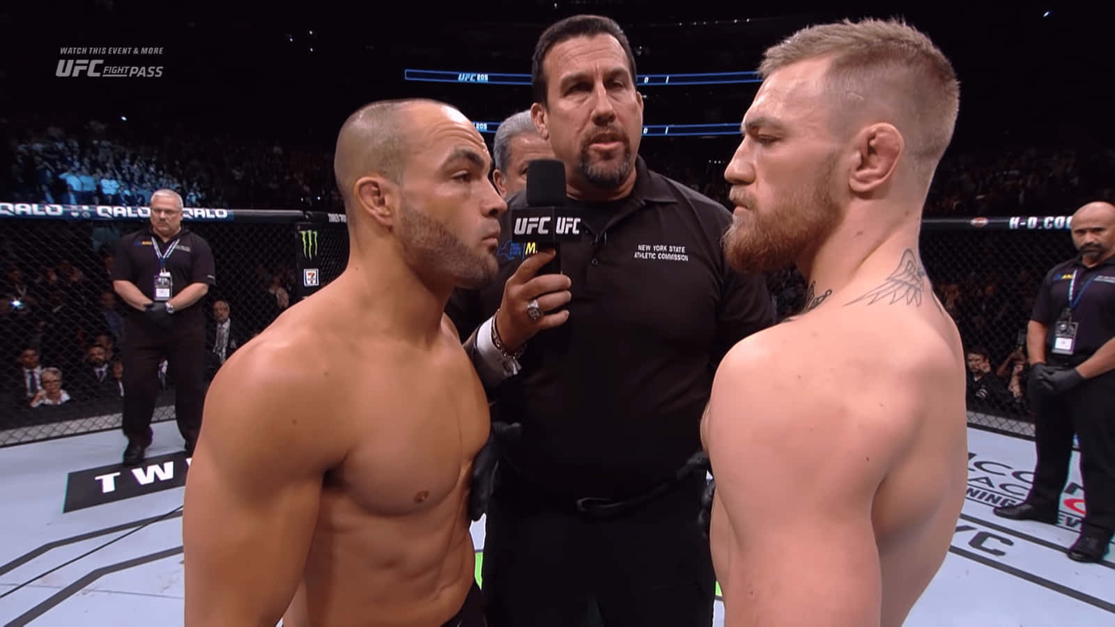UFC 桌布 壁紙 — 兩名肌肉發達的拳手在UFC八角籠中對峙，裁判在他們之間拿著麥克風。