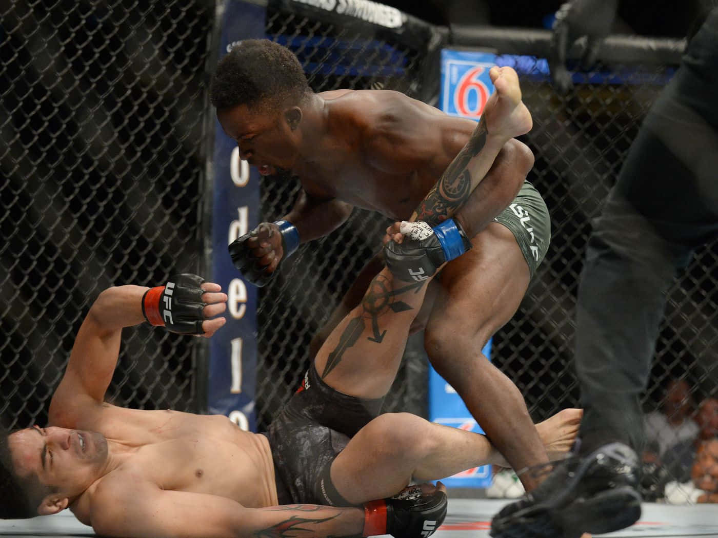 UFC 桌布 壁紙 — 兩名肌肉發達的拳手在UFC八角籠內激烈纏鬥，背景有鐵絲網和模糊的觀眾。