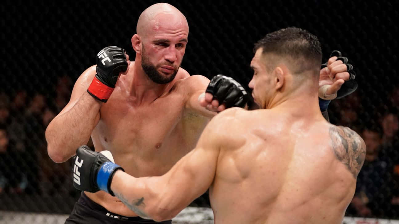 MMA 桌布 壁紙 — 兩名肌肉發達的拳手在UFC八角籠中激烈交鋒，汗水飛濺，其中一人向對手面部打出強力一拳。