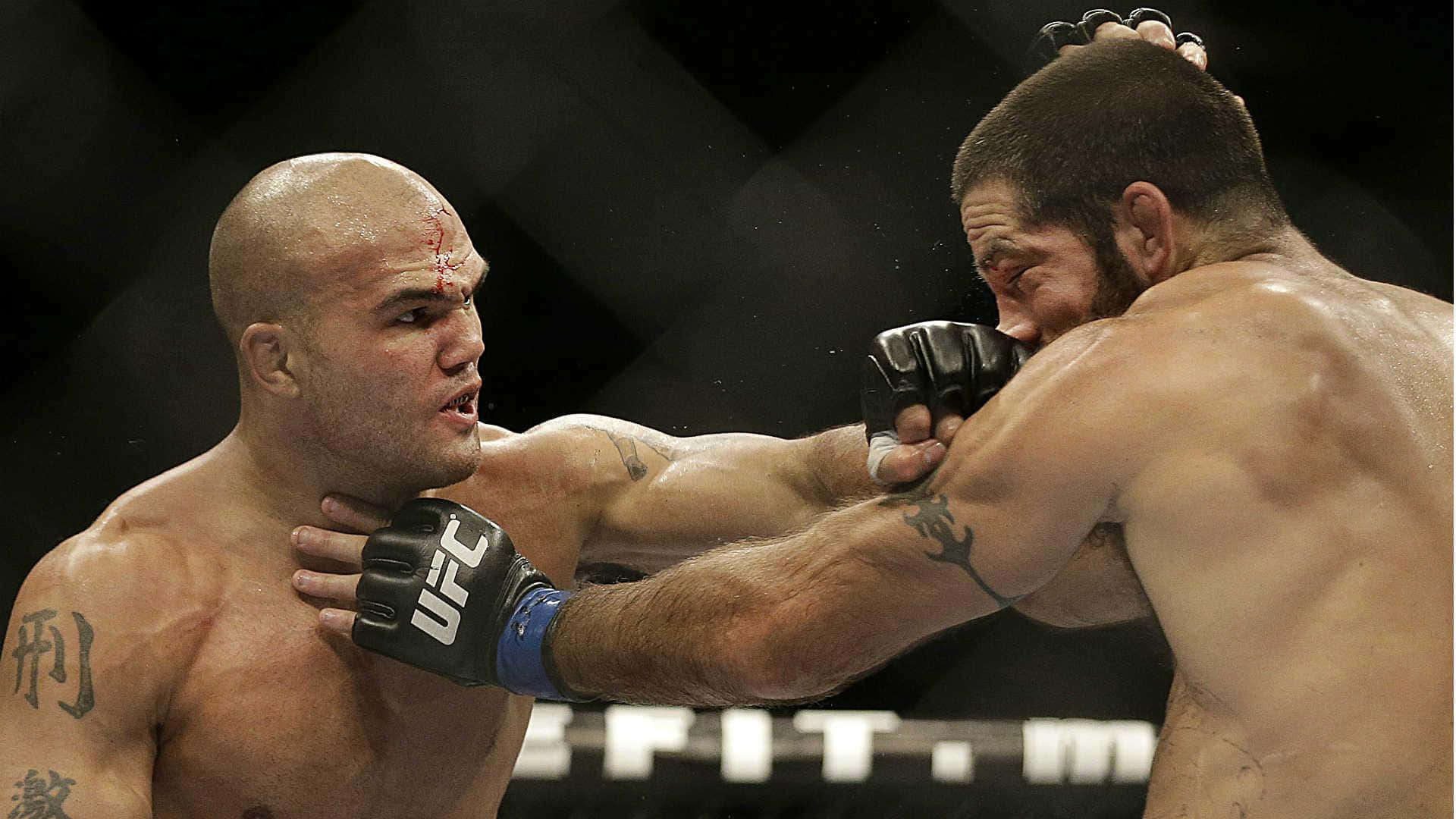 MMA 桌布 壁紙 — 兩名肌肉發達的拳手在UFC八角籠中交鋒，其中一人打出兇猛一拳，另一人額頭流血，在明亮的場館燈光下。