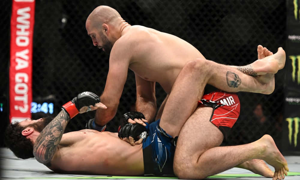 MMA 桌布 壁紙 — 兩名肌肉發達的拳手在一個帶有明顯品牌標誌和計時器的MMA八角籠內進行激烈的纏鬥。