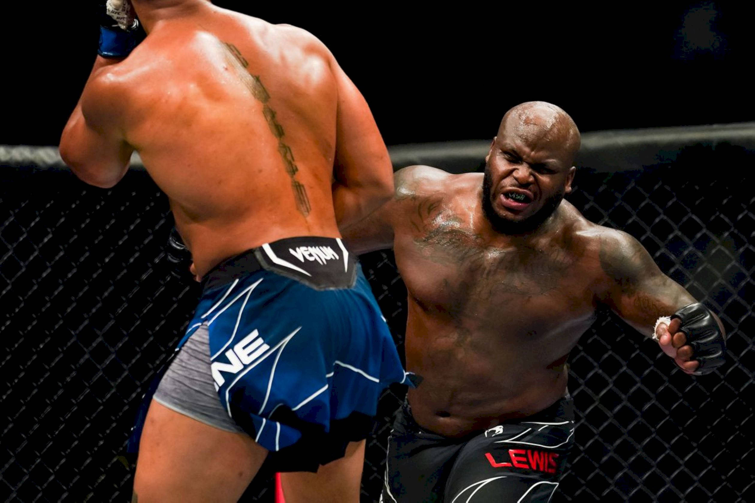 桌布 壁紙 — 兩名肌肉發達的拳手在光線昏暗、帶有鐵絲網圍欄的MMA八角籠內激烈交鋒。