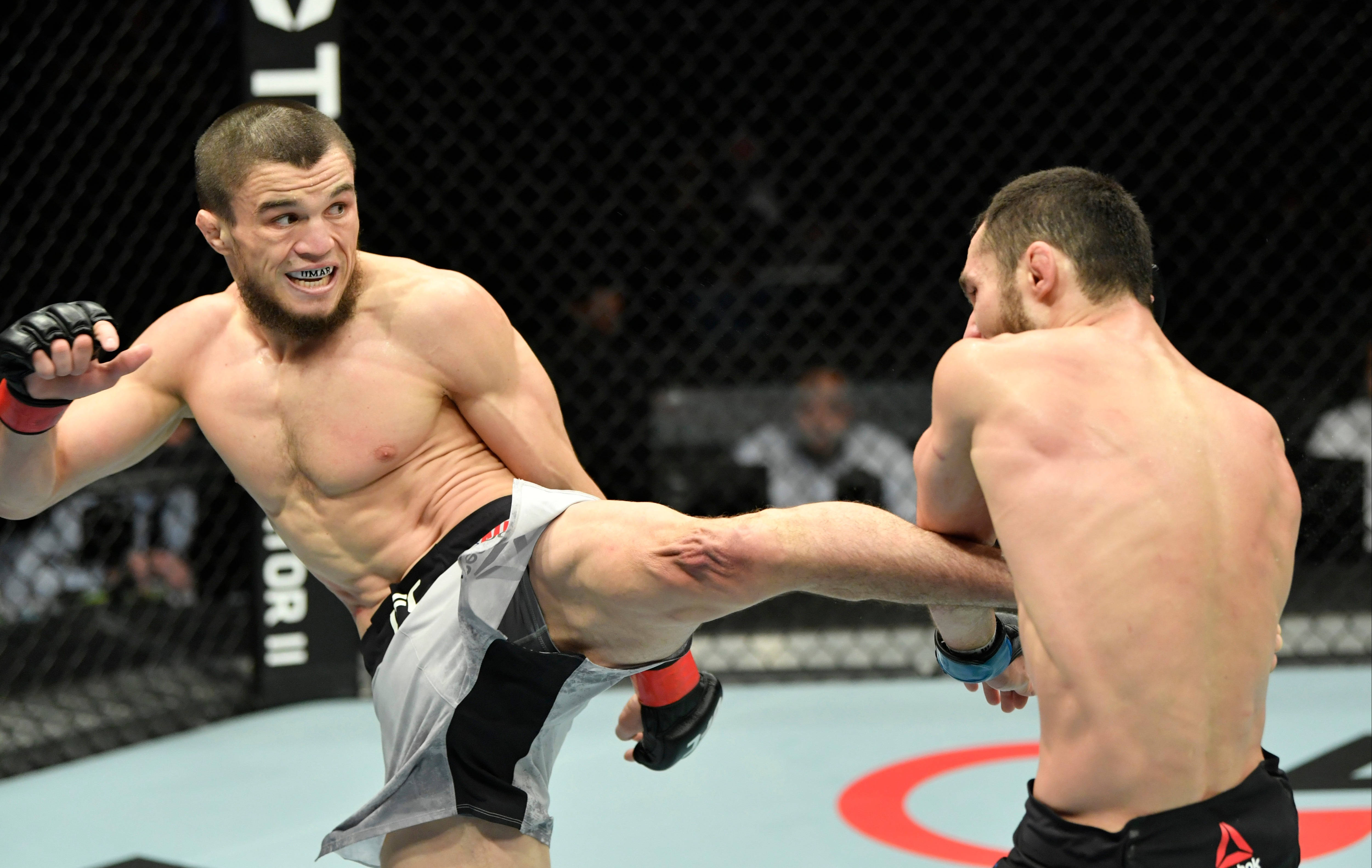 MMA 桌布 壁紙 — 兩名肌肉發達的拳手在八角籠中交鋒，一人使出高踢，另一人阻擋，展開緊張的MMA比賽。