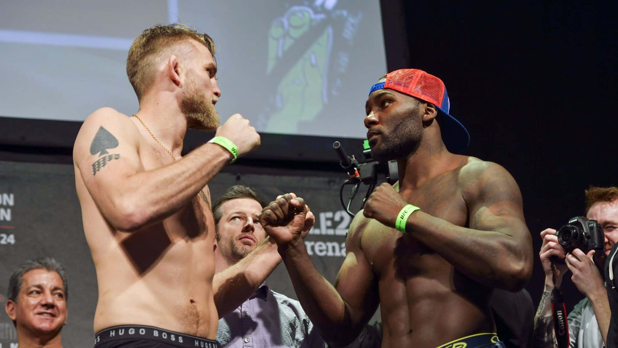 UFC 桌布 壁紙 — 兩名肌肉發達的拳手在明亮燈光下的舞台上鎖拳，攝影師捕捉這緊張時刻。