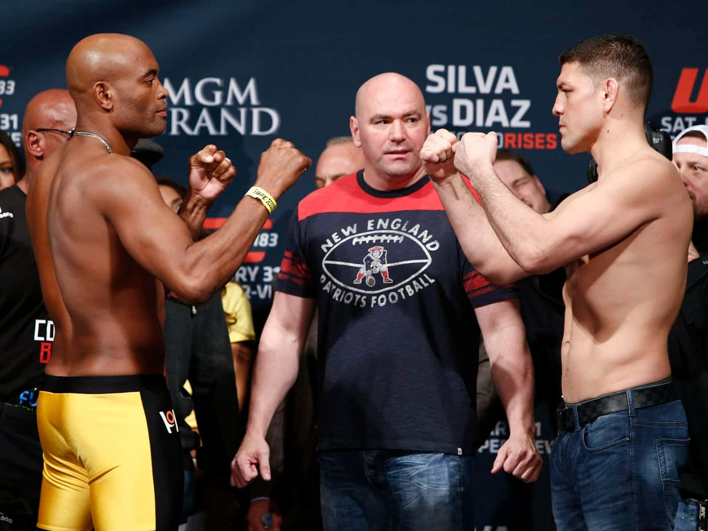 UFC 桌布 壁紙 — 兩名肌肉發達的拳手在明亮的場館燈光下，在緊張的賽前稱重中對峙，中間站著一名裁判。