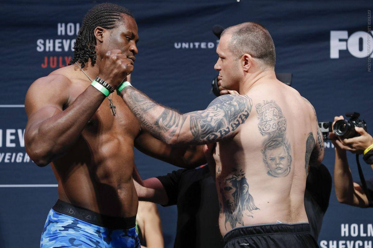 MMA 桌布 壁紙 — 兩名肌肉發達的拳手在明亮的場館燈光下，帶著強烈的表情和可見的紋身，在稱重時對峙。