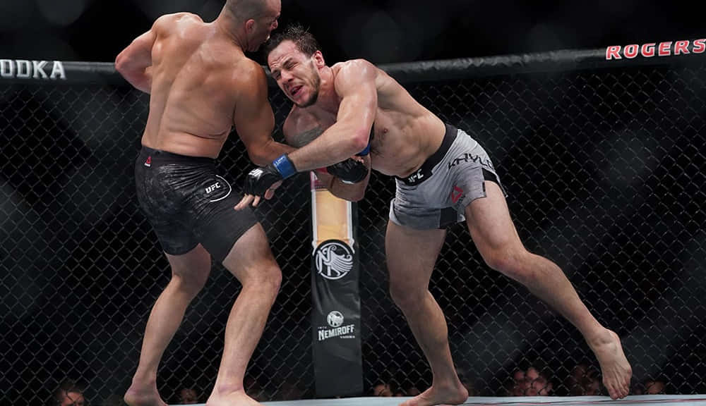 桌布 壁紙 — 兩名肌肉發達的拳手在明亮的場館燈光下於UFC八角籠中激烈纏鬥。