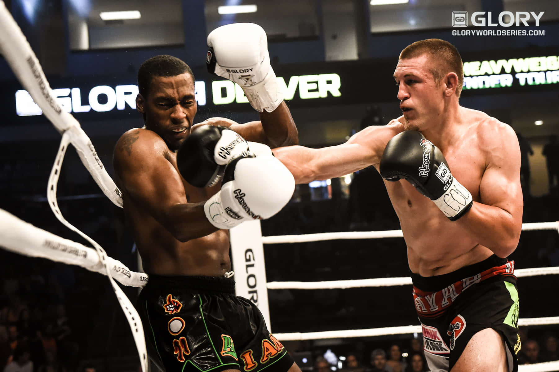 MMA 桌布 壁紙 — 兩名肌肉發達的拳手在明亮的擂台上交鋒，其中一人在GLORY踢拳比賽中向對手面部擊出強力一拳。