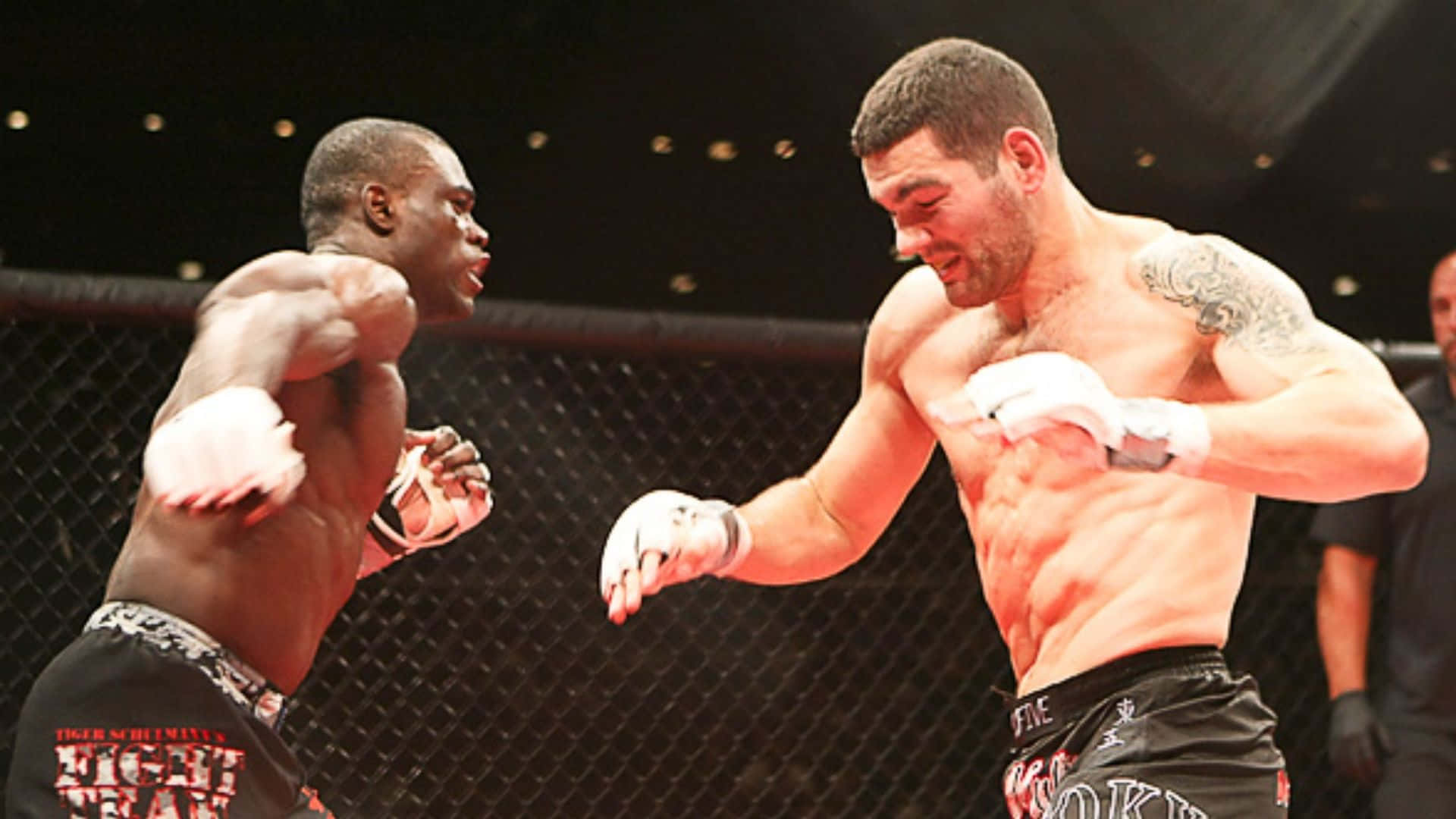 MMA 桌布 壁紙 — 兩名肌肉發達的拳手在明亮的競技場燈光下，在籠中進行激烈的綜合格鬥比賽。