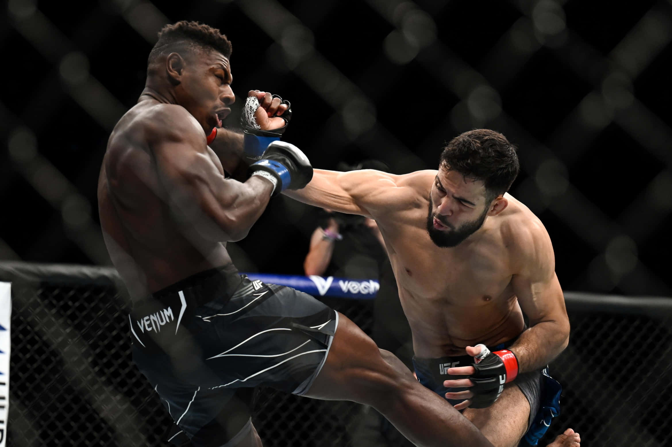UFC 桌布 壁紙 — 兩名肌肉發達的拳手在昏暗的八角籠內激烈交鋒，背景是模糊的籠網。