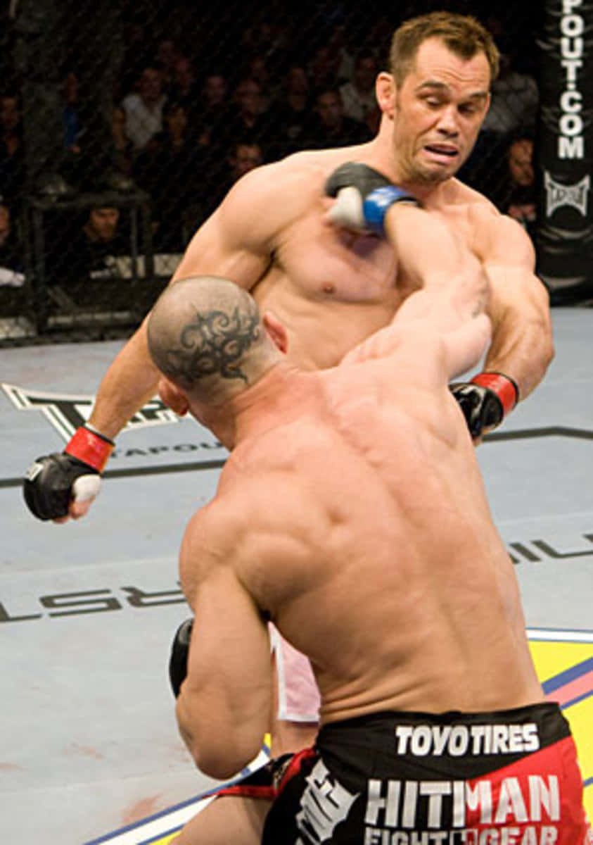UFC 桌布 壁紙 — 兩名肌肉發達的拳手在燈光通明的MMA八角籠中激烈纏鬥，背景有觀眾。