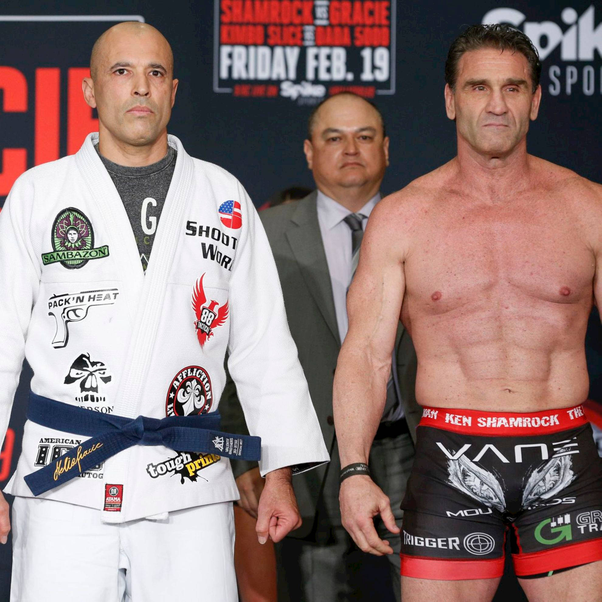 MMA 桌布 壁紙 — 兩名肌肉發達的拳手在稱重活動中面向前方站立，一人身穿帶有補丁的白色道服，另一人身穿帶紅色飾邊的黑色短褲。