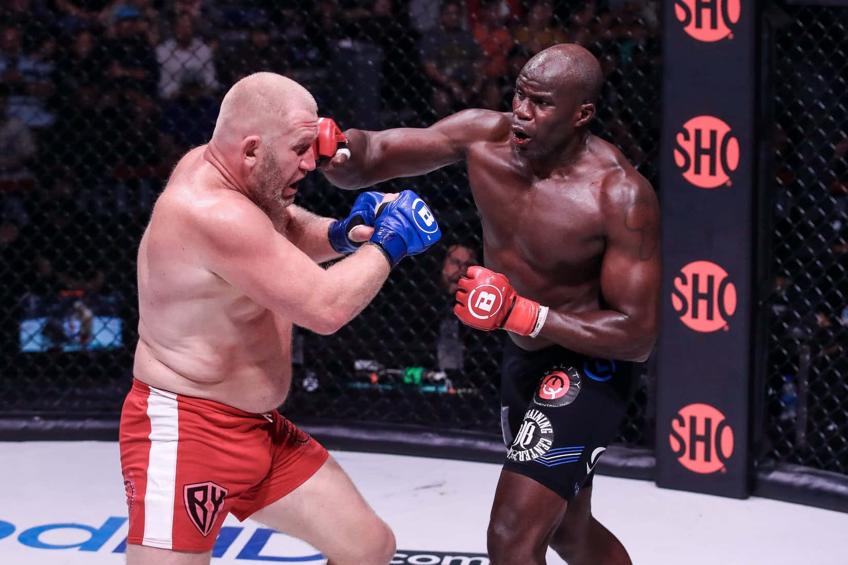 MMA 桌布 壁紙 — 兩名肌肉發達的拳手在籠中激烈交鋒，其中一人在高風險的MMA比賽中向對方臉部打出強力一拳。