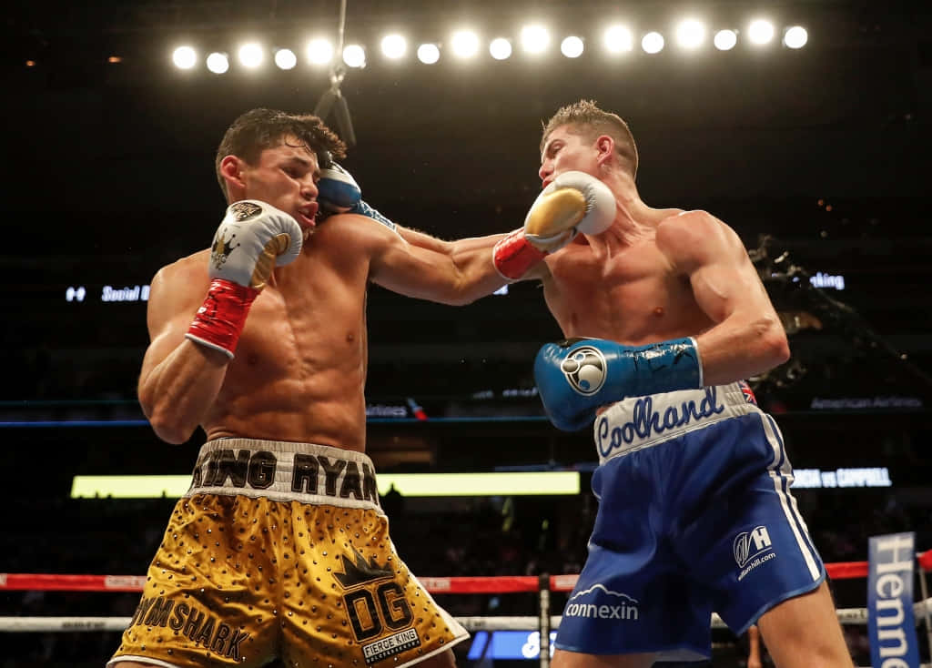 Ryan Garcia 桌布 壁紙 — 兩名肌肉發達的拳擊手在燈光明亮的擂台上交鋒，其中一人擊中對方的臉部，觀眾席的燈光在上方閃耀。