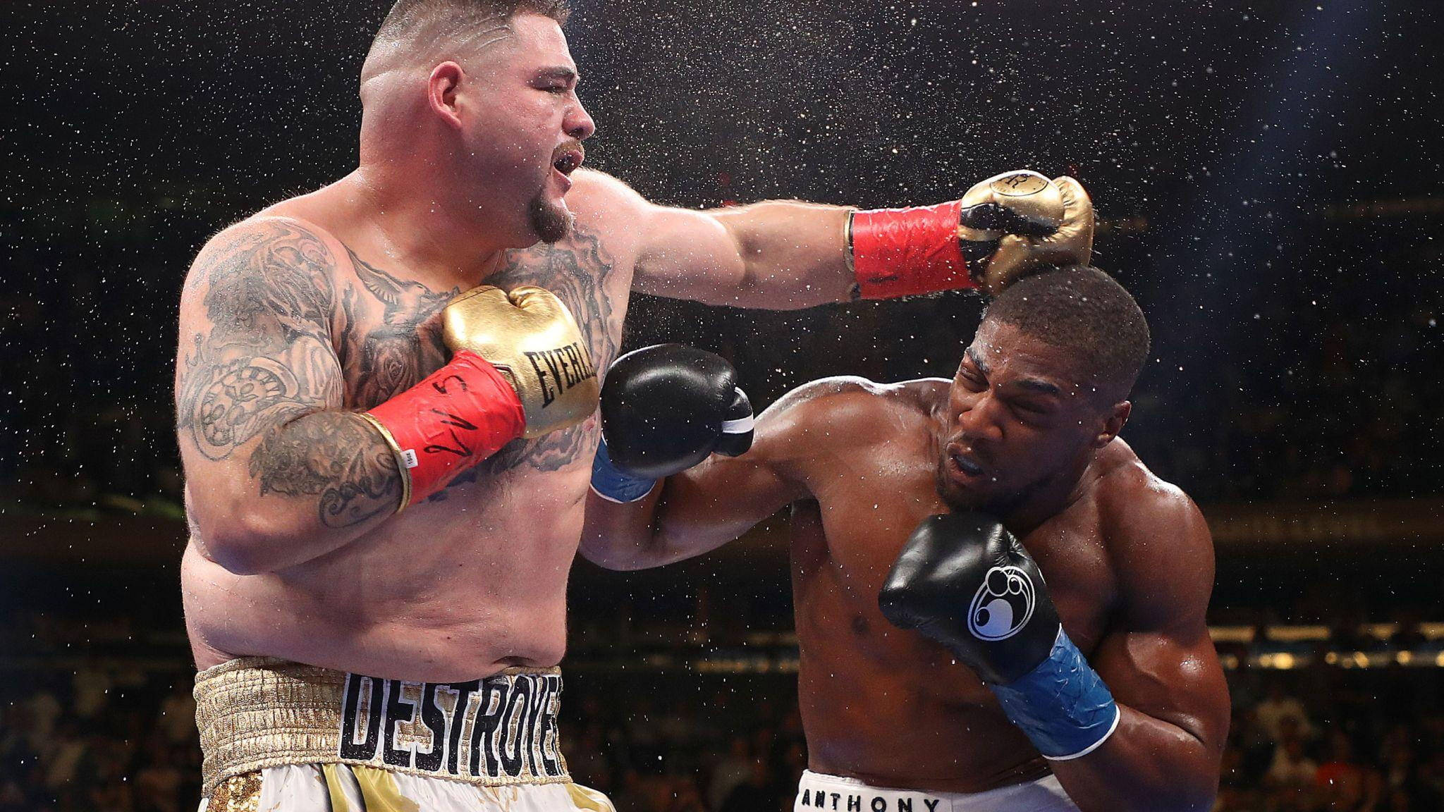 Anthony Joshua 桌布 壁紙 — 兩名肌肉發達的拳擊手在雨水飛濺的擂台上交鋒，其中一人重拳擊中對方的頭部。