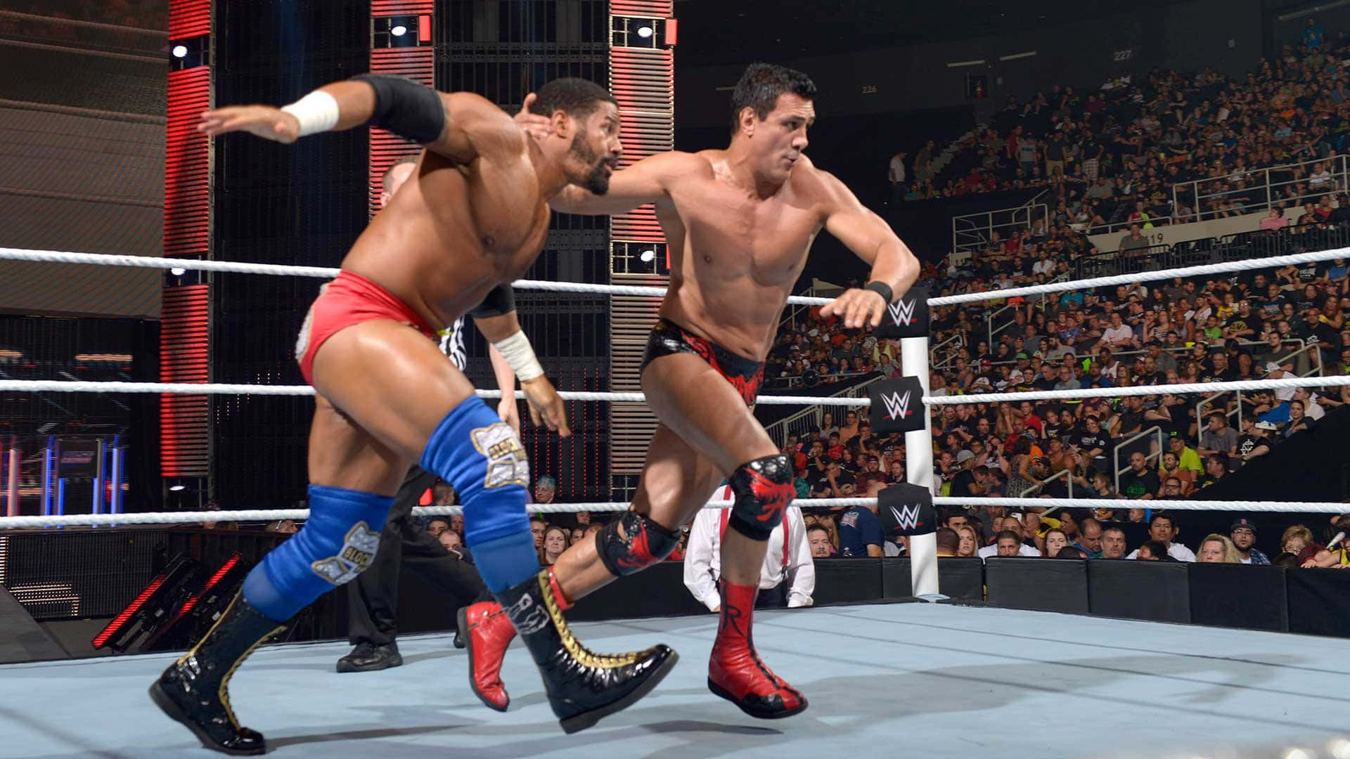 WWE 桌布 壁紙 — 兩名肌肉發達的摔角手在WWE擂台上交鋒，背景是咆哮的人群。