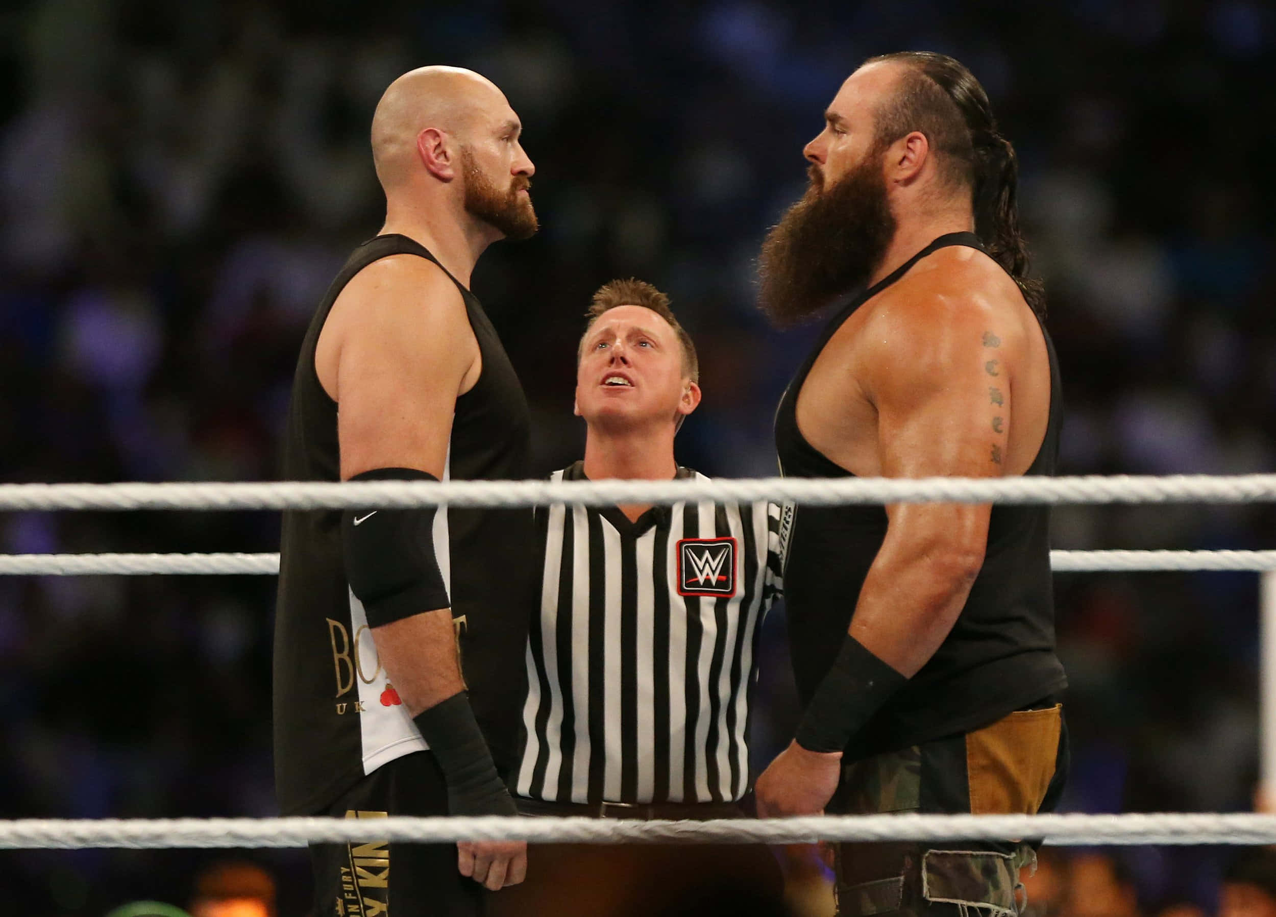 WWE 桌布 壁紙 — 兩名肌肉發達的摔角手在摔角台上隔著裁判互相怒視。