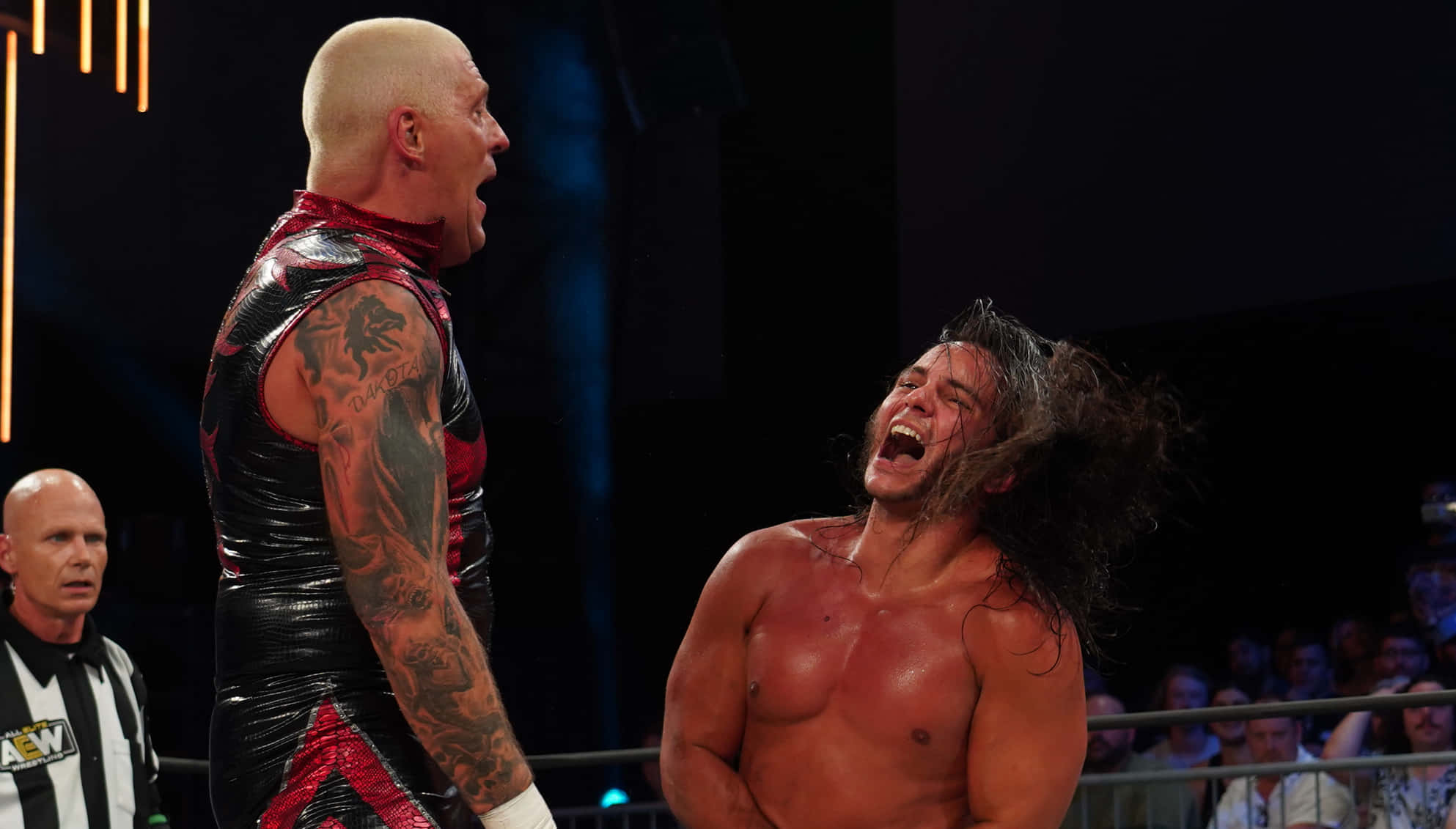 WWE 桌布 壁紙 — 兩名肌肉發達的摔角手在擂台上，其中一名有紋身的摔角手向對手咆哮，對手在明亮的場館燈光下痛苦尖叫。