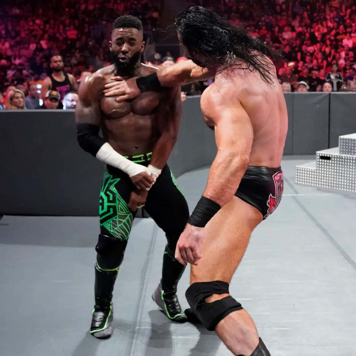 WWE 桌布 壁紙 — 兩名肌肉發達的摔角手在擂台上交鋒，周圍是紅光籠罩下咆哮的人群。