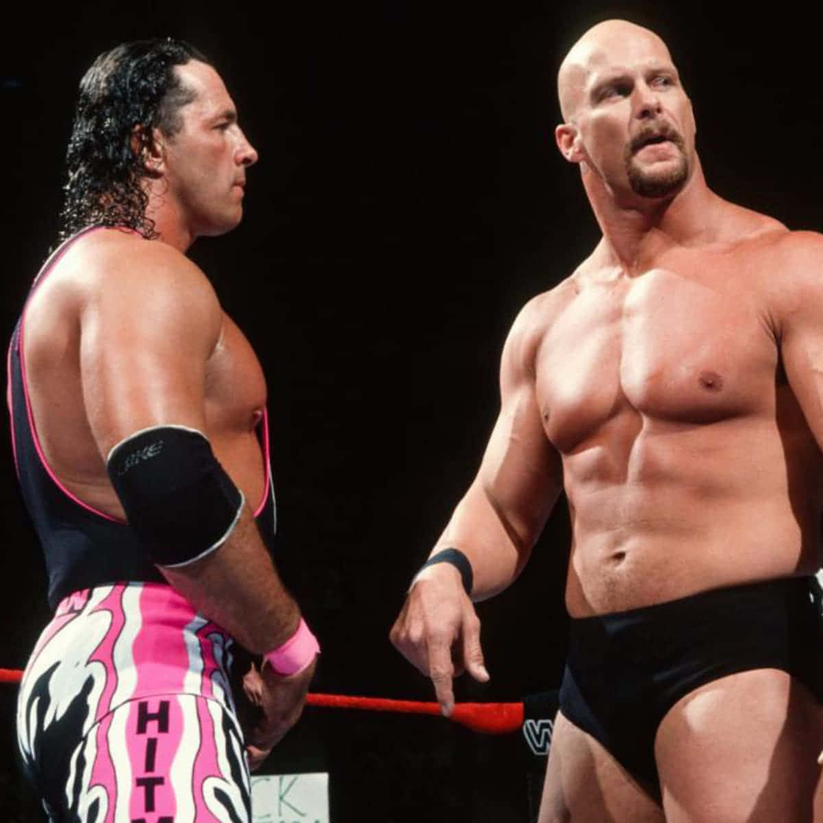 WWE 桌布 壁紙 — 兩名肌肉發達的摔角手在擂台上對峙，一人穿著粉紅、黑、白色摔角褲，另一人穿著黑色摔角褲，在明亮的場館燈光下。