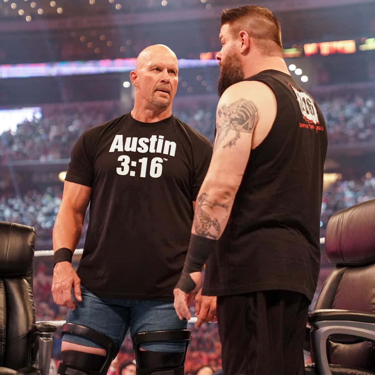 WWE 桌布 壁紙 — 兩名肌肉發達的摔角手在擂台上對峙，身後是座無虛席的競技場，在明亮的競技場燈光下。