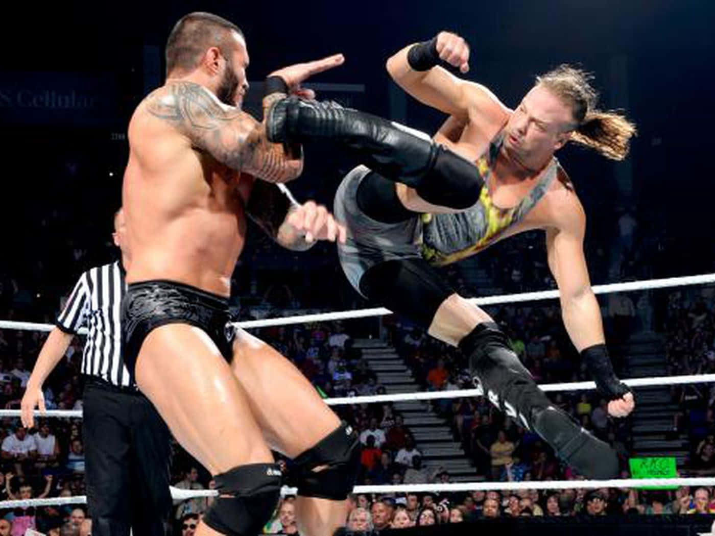 WWE 桌布 壁紙 — 兩名肌肉發達的摔角手在擂台上碰撞，一人凌空踢腿，觀眾在明亮的場館燈光下緊張觀看。