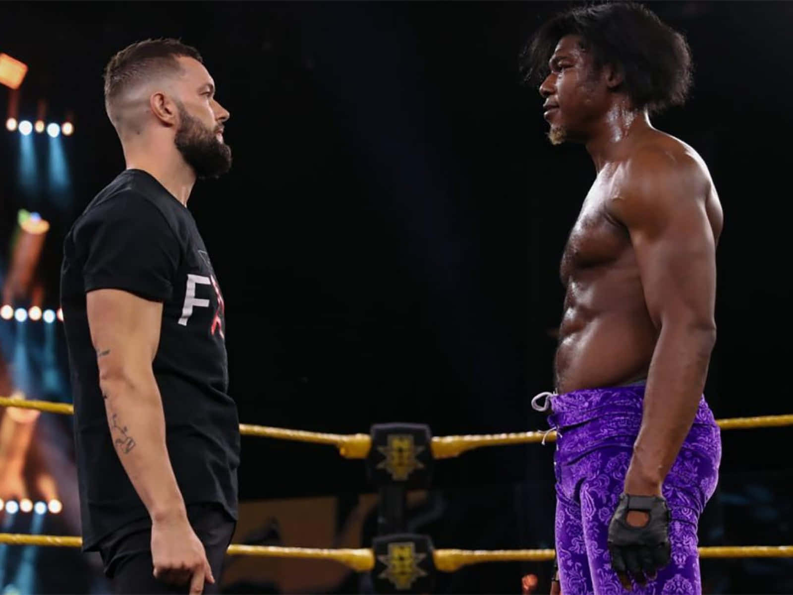 WWE 桌布 壁紙 — 兩名肌肉發達的摔角手在明亮的擂台上，在戲劇性的舞台燈光下對峙。