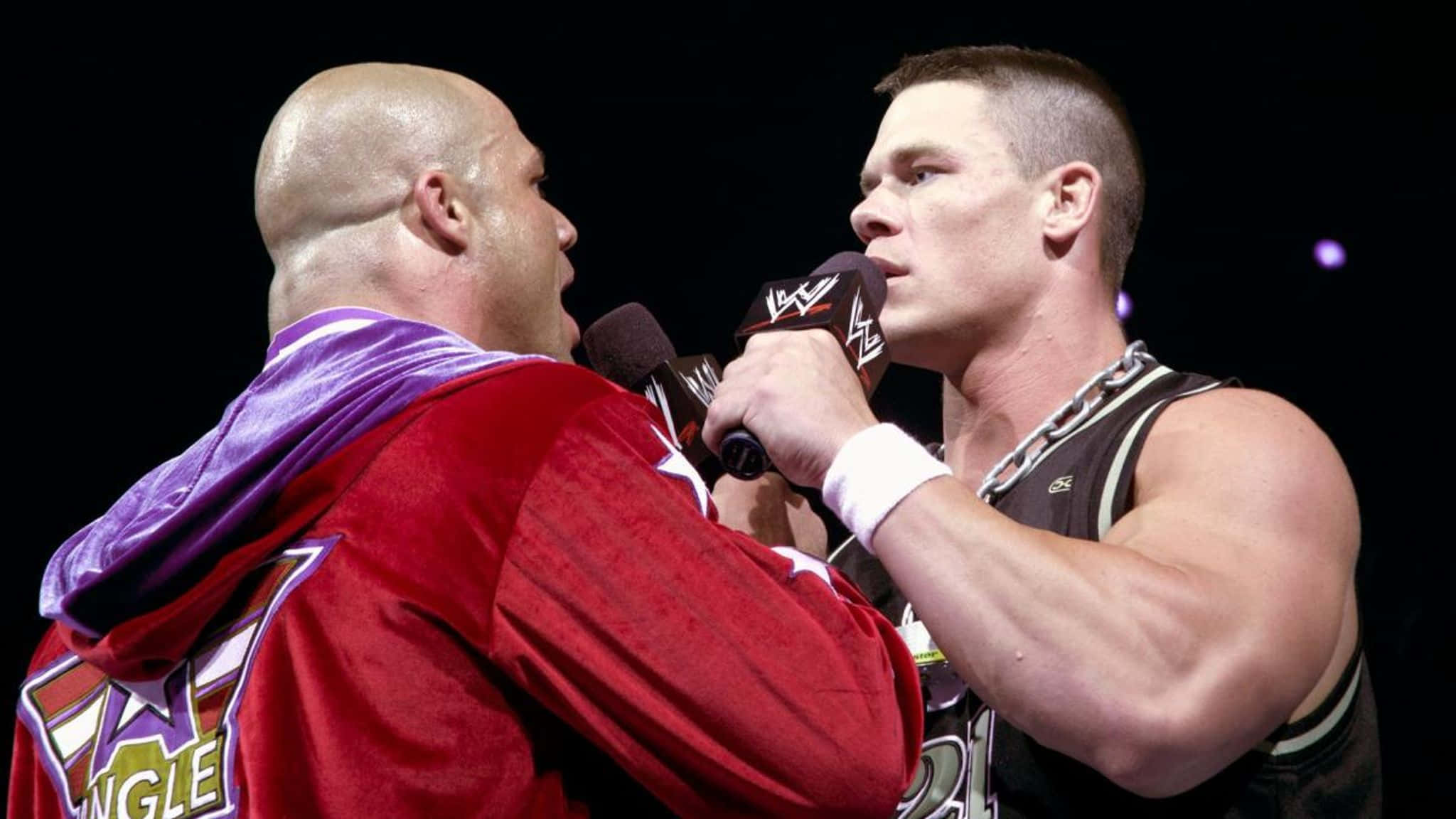 WWE 桌布 壁紙 — 兩名肌肉發達的摔角手在明亮的舞台燈光下手持麥克風激烈對峙。