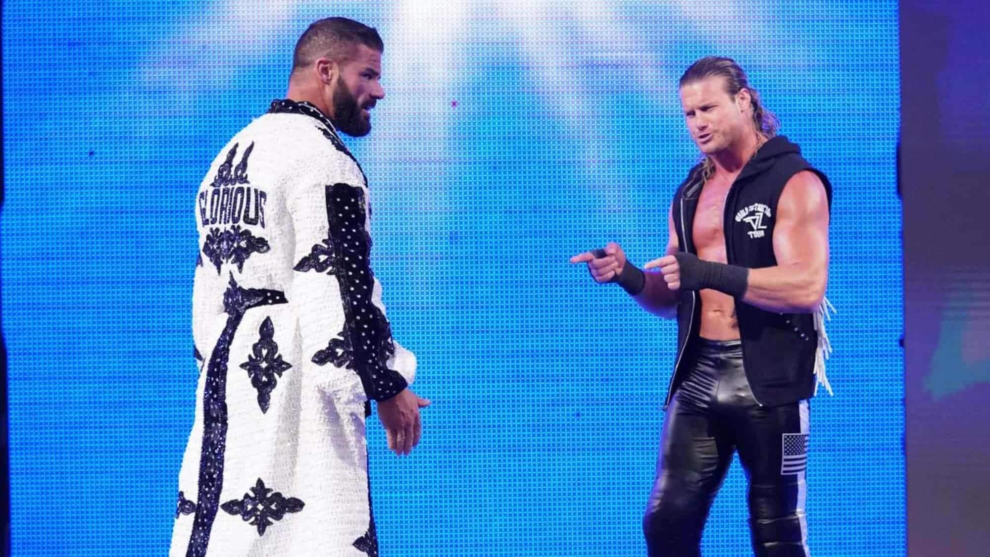 摔角 桌布 壁紙 — 兩名肌肉發達的摔角手在明亮的藍色舞台上對峙，一人身穿白色長袍，另一人穿著黑色皮革。