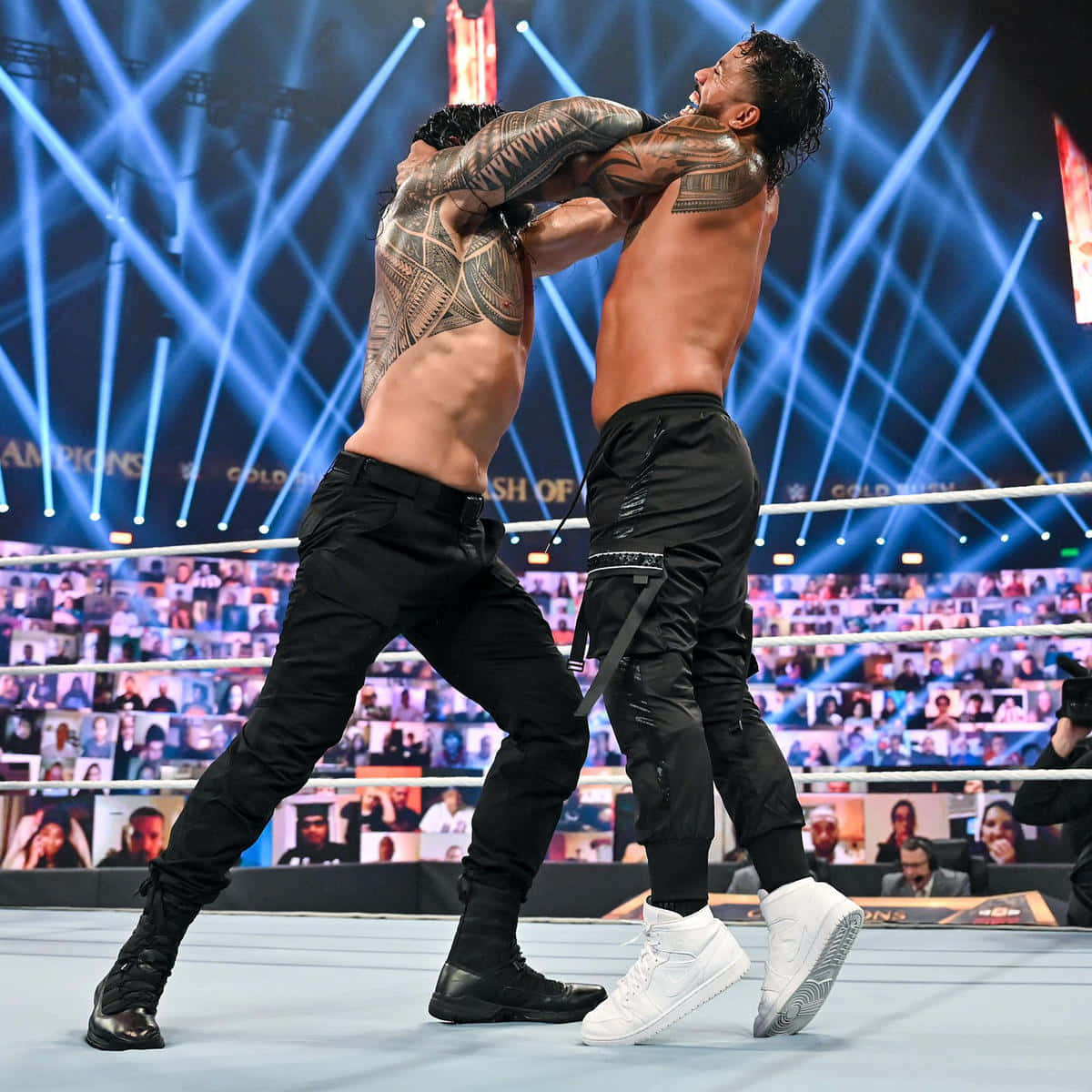 Roman Reigns 桌布 壁紙 — 兩名肌肉發達的摔角手在明亮的藍色舞台燈光下於擂台上激烈纏鬥，背景中可見一群粉絲。