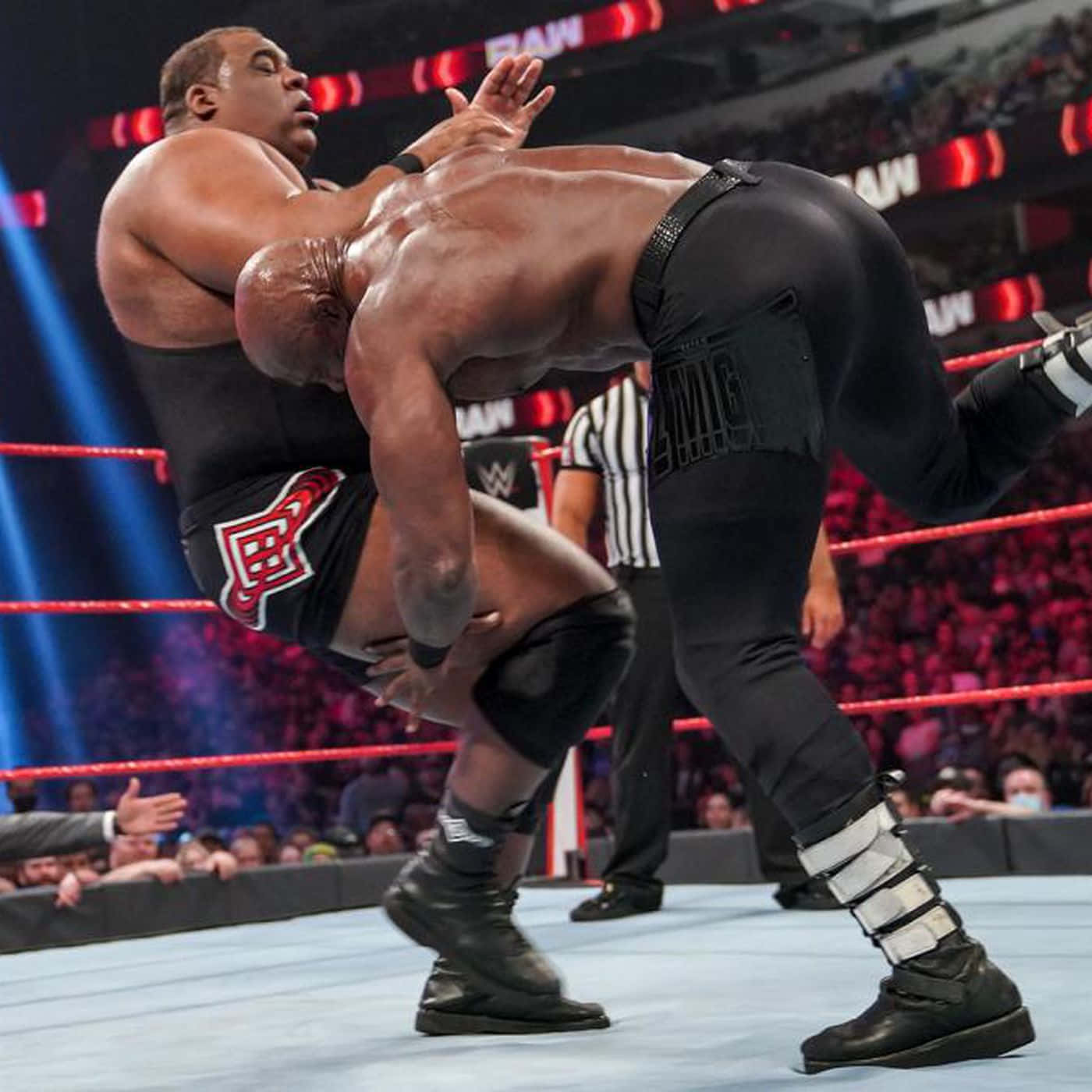 WWE 桌布 壁紙 — 兩名肌肉發達的摔角手在燈光明亮的擂台上激烈纏鬥，背景有裁判和歡呼的人群。