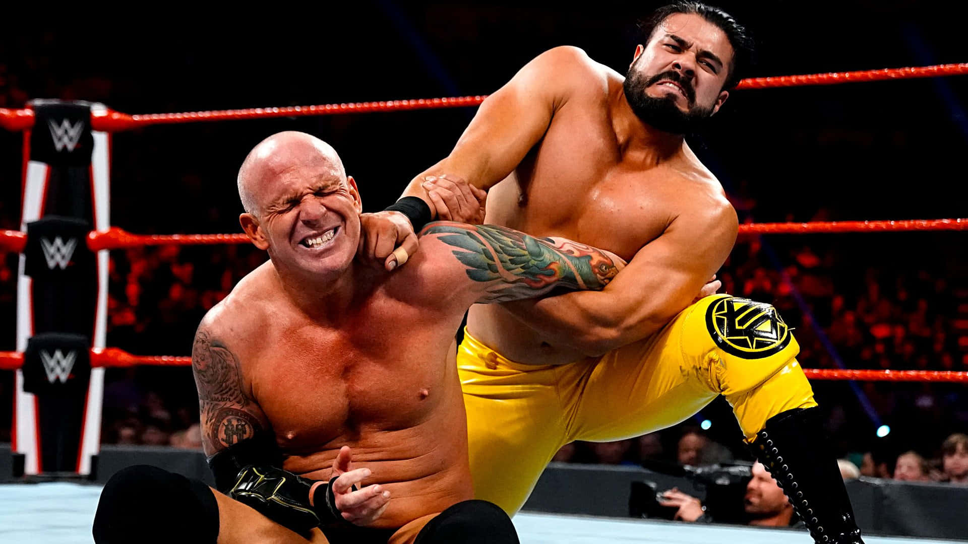 WWE 桌布 壁紙 — 兩名肌肉發達的摔角手在燈光明亮的擂台上激烈纏鬥，擂台有紅色繩索和WWE標誌。