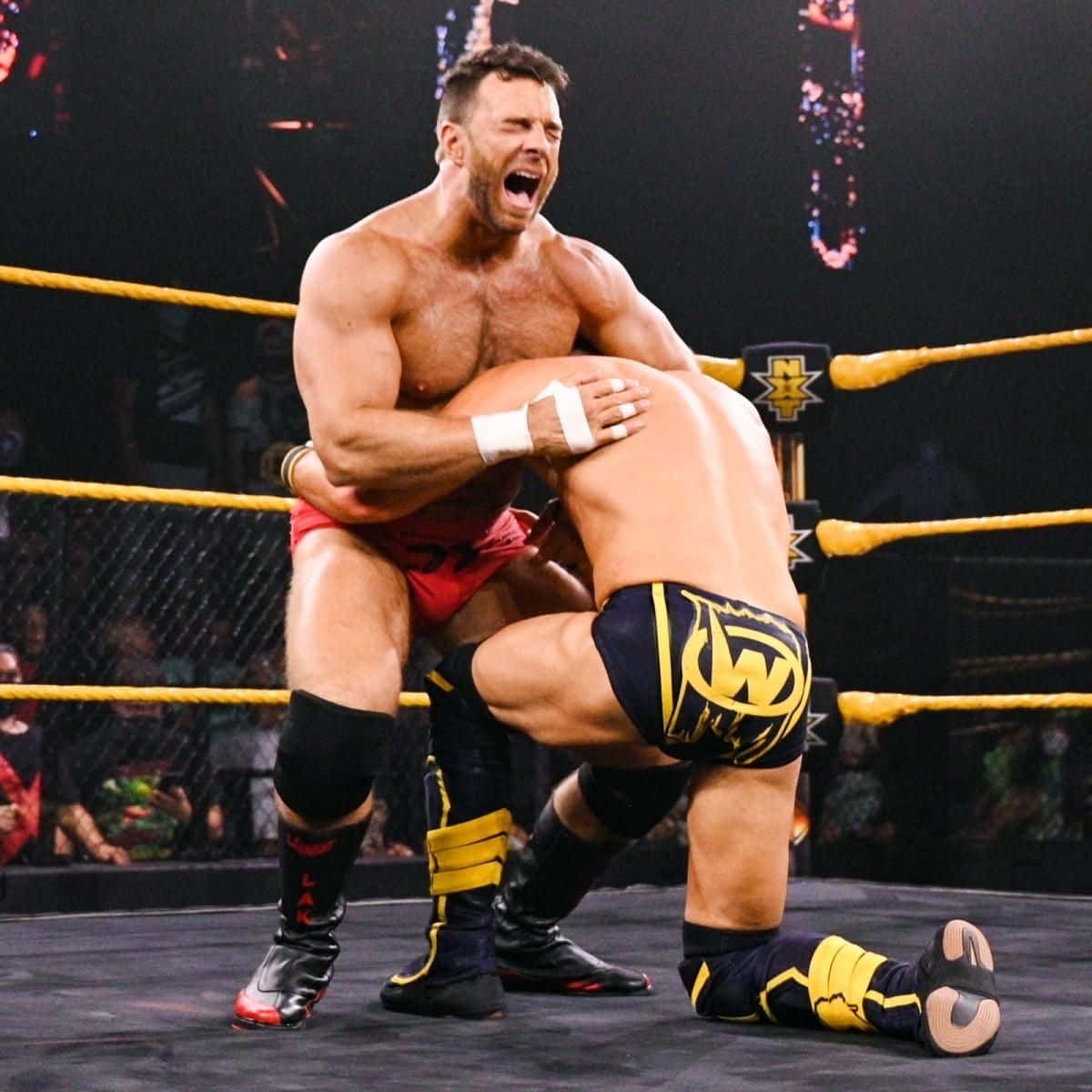 WWE 桌布 壁紙 — 兩名肌肉發達的摔角手在燈光明亮的擂台上激烈纏鬥，擂台有黃色繩索，背景是歡呼的人群。