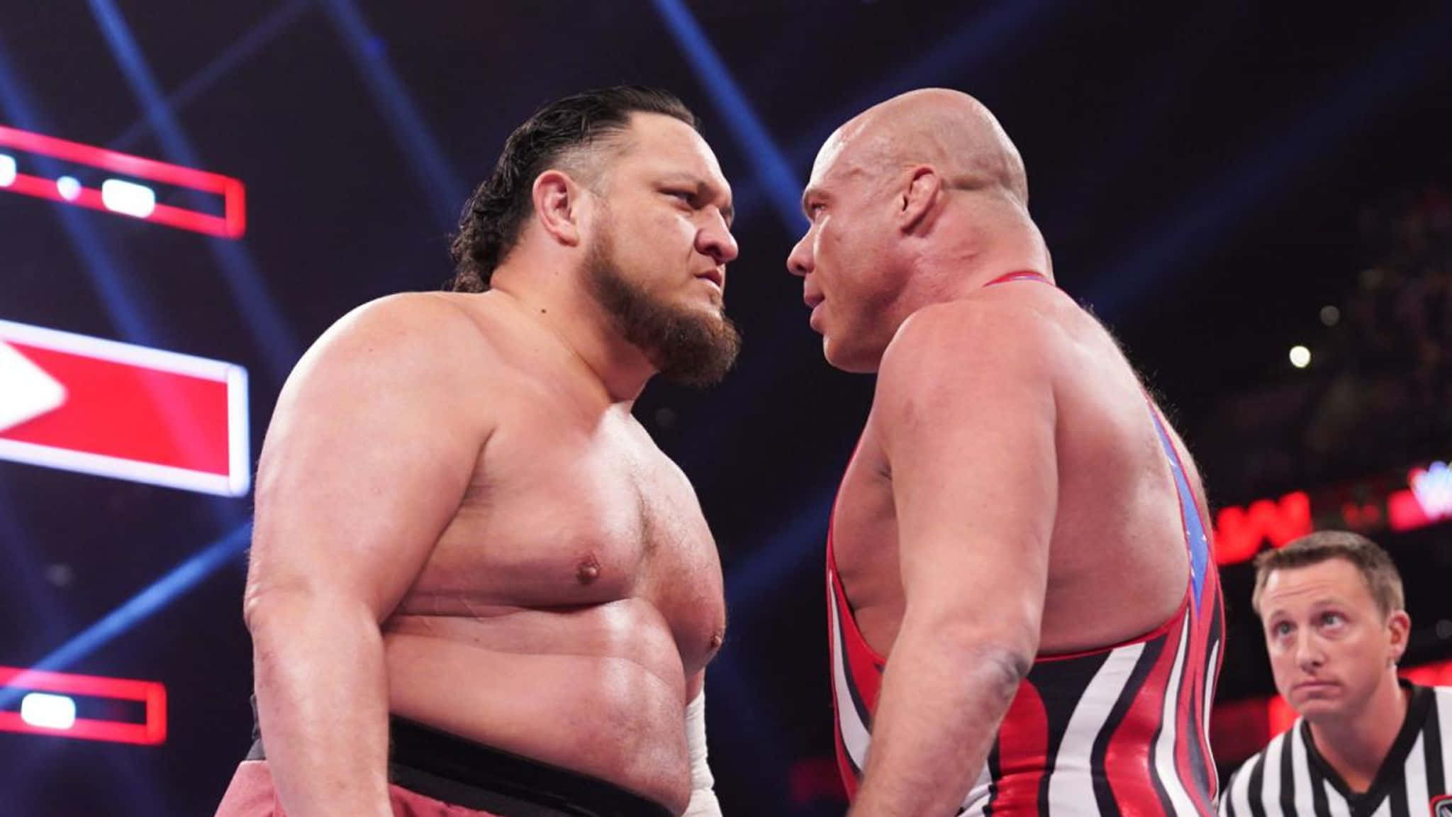 WWE 桌布 壁紙 — 兩名肌肉發達的摔角手在燈光明亮的擂台上互相怒視，裁判在旁觀看。