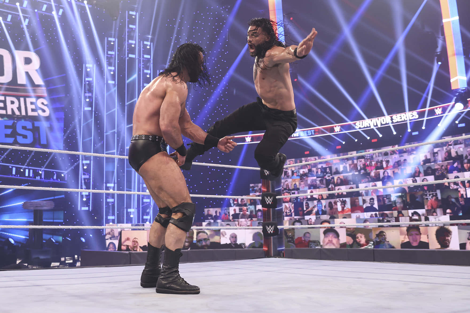 WWE 桌布 壁紙 — 兩名肌肉發達的摔角手在燈光明亮的擂台上對決，藍色聚光燈照射，身後屏幕上有大批粉絲。