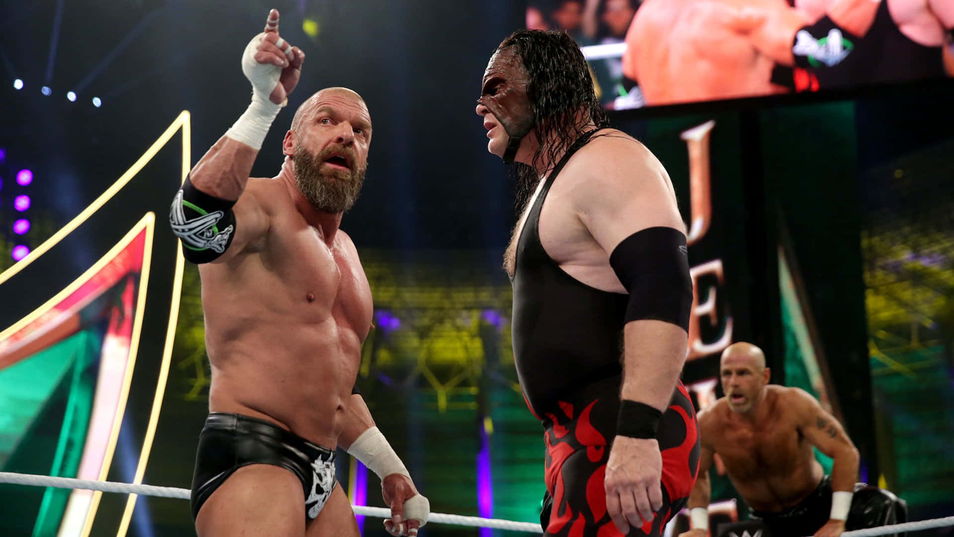 WWE 桌布 壁紙 — 兩名肌肉發達的摔角手在燈光明亮的擂台上對峙，背景有戲劇性的舞台燈光和第三名摔角手。