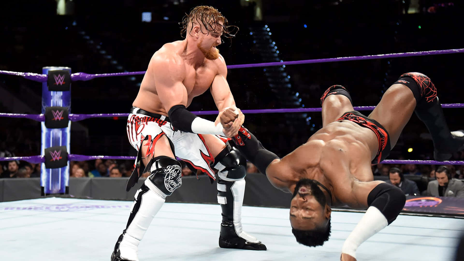 WWE 桌布 壁紙 — 兩名肌肉發達的摔角手在燈光明亮的擂台上激烈纏鬥，擂台有紫色繩索，背景是歡呼的人群。