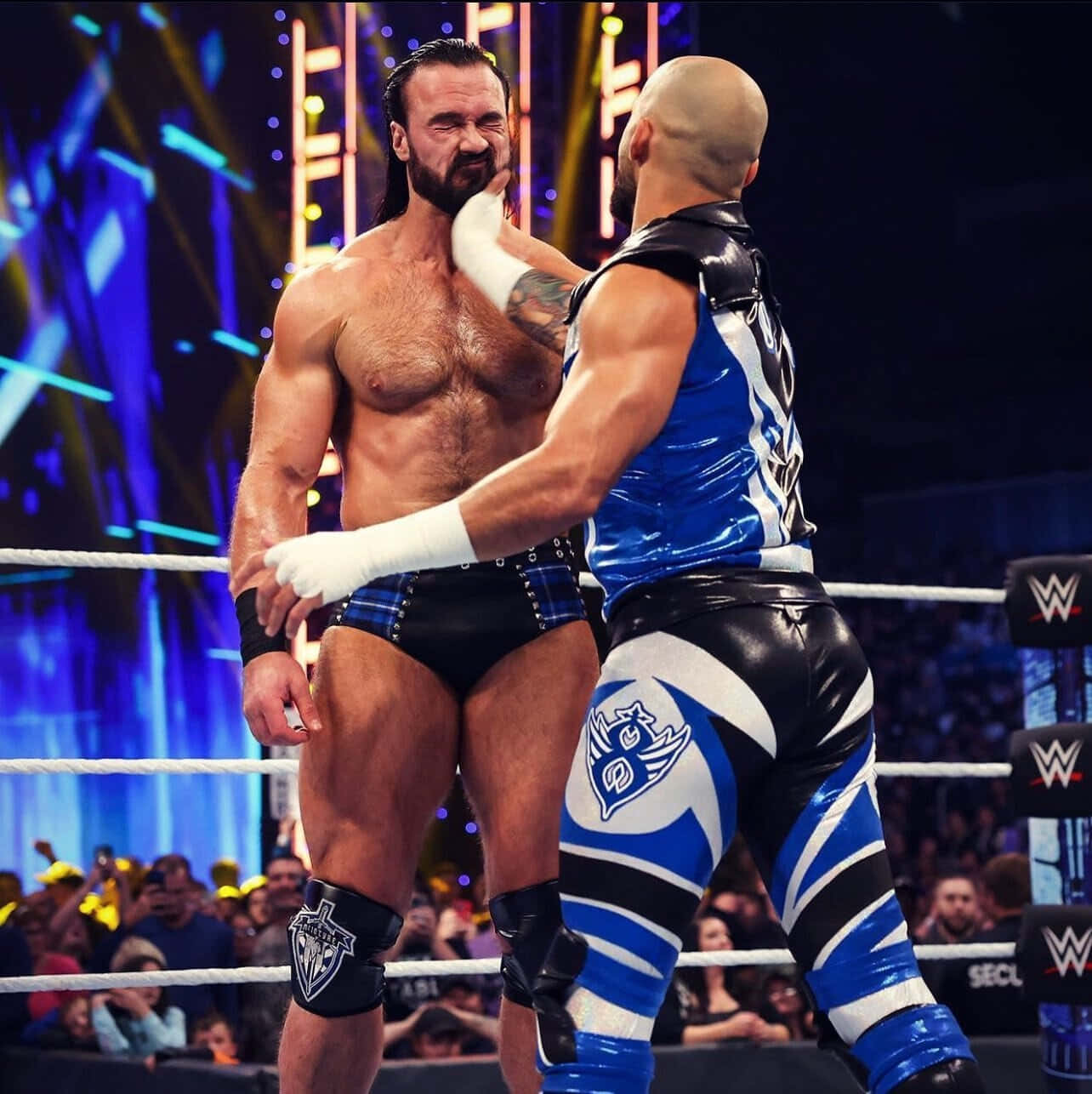 WWE 桌布 壁紙 — 兩名肌肉發達的摔角手在燈光明亮的擂台上激烈纏鬥，背景有發光的藍色燈光和歡呼的粉絲。