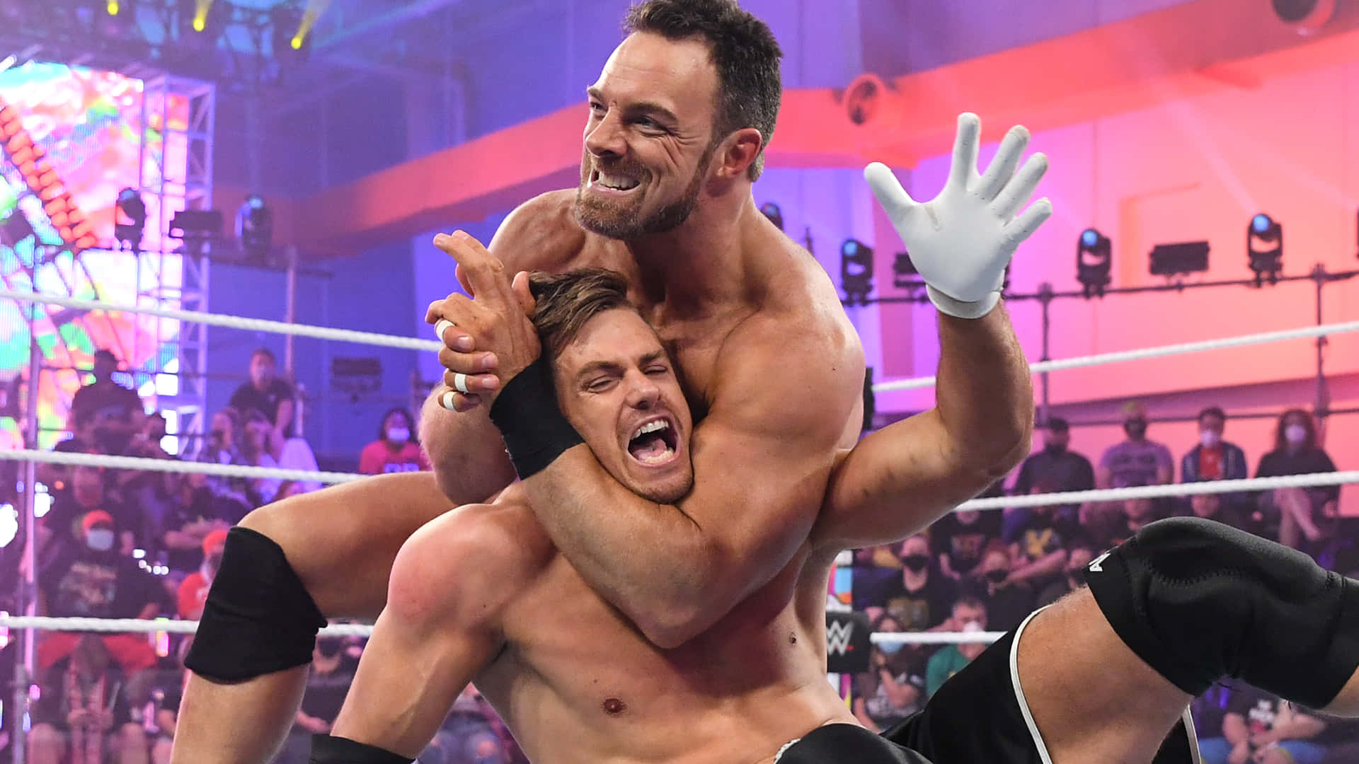 WWE 桌布 壁紙 — 兩名肌肉發達的摔角手在燈光璀璨的擂台上激烈纏鬥，周圍是歡呼的粉絲和色彩繽紛的舞台燈光。