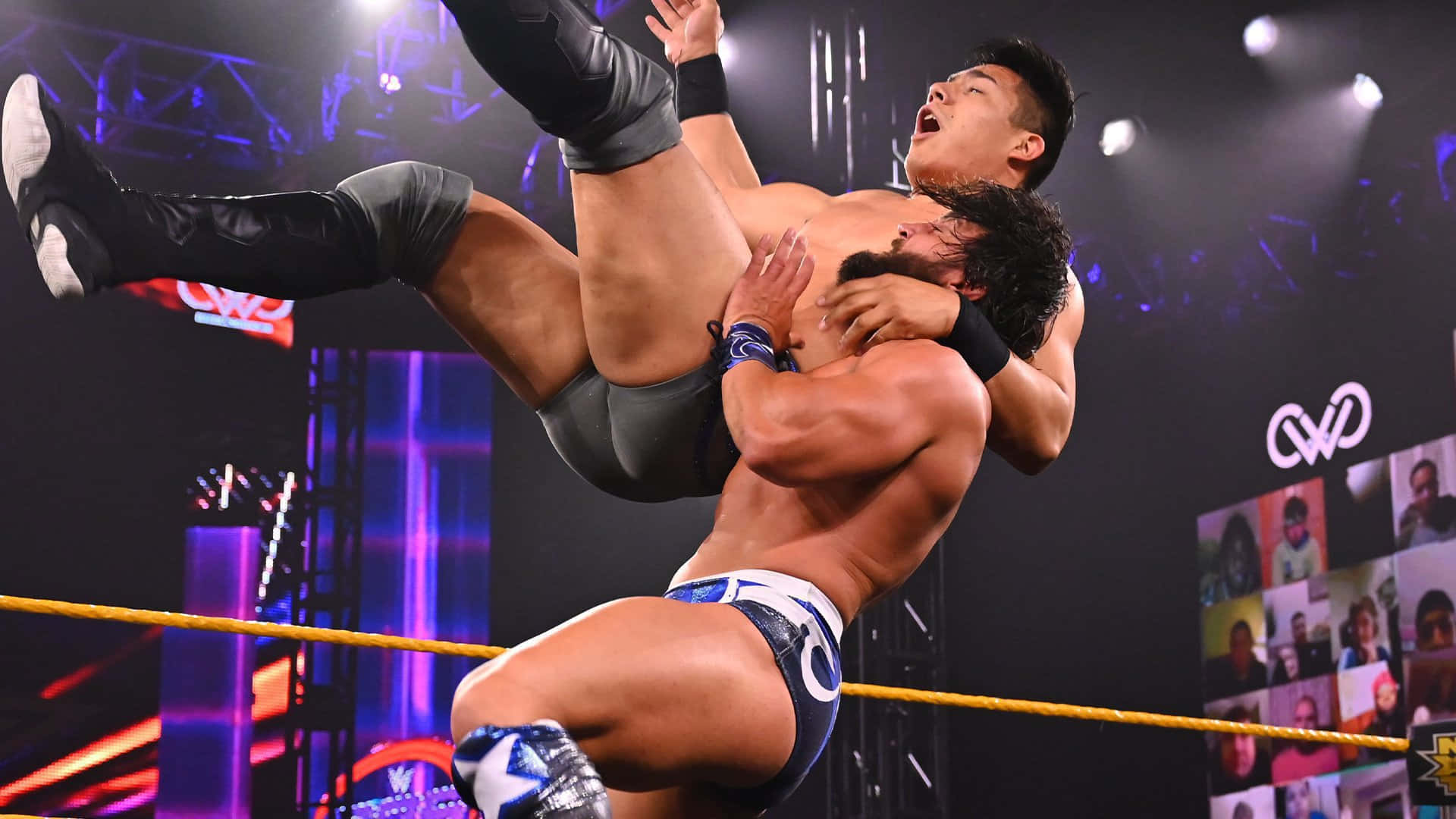 WWE 桌布 壁紙 — 兩名肌肉發達的摔角手在燈光璀璨的擂台上進行激烈的空中纏鬥。